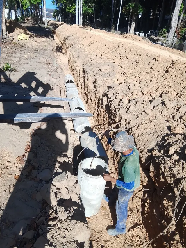 Vala aberta com tubulação de drenagem pluvial sendo assentada