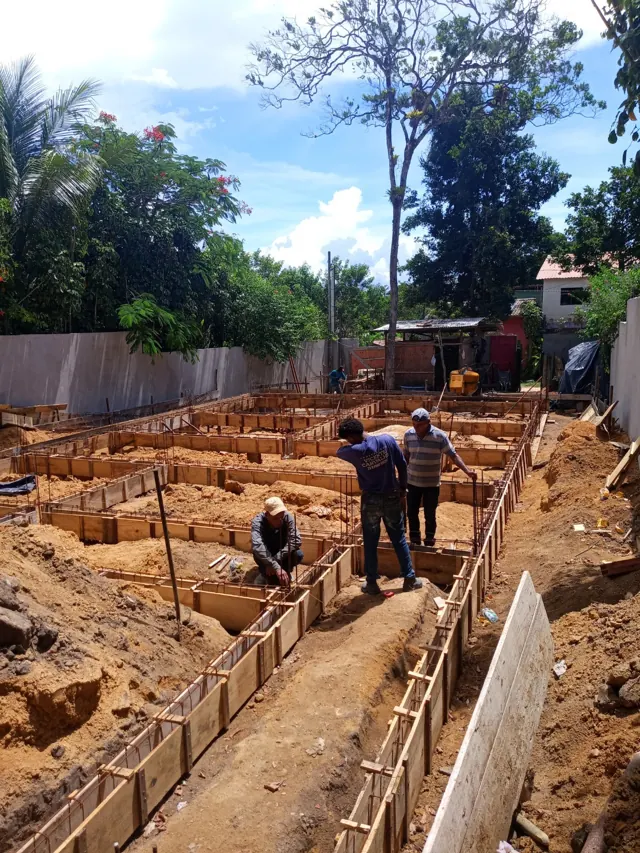 Equipe executando vigas baldrame com formas de madeira em terreno